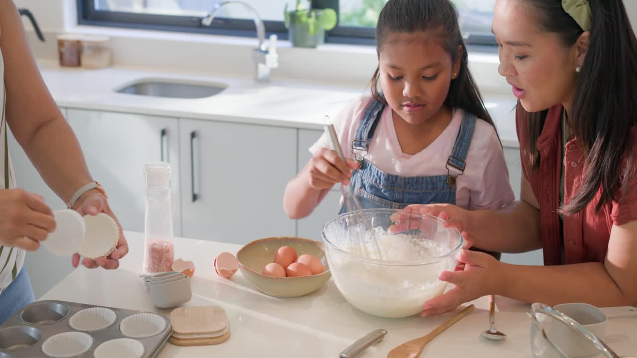 Keluarga multietnis memanggang muffin di meja dapur, anak mengocok adonan di mangkuk kaca, orang dewasa melapisi loyang.