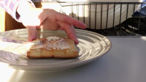 male hand cutting buttered crumpet in half on plate