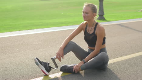 mujer con extremidad artificial sentada en la carretera. chica relajándose después de entrenar en el parque