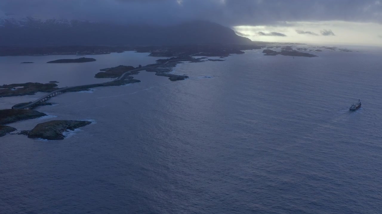 Uma tomada aérea ampla de um navio de carga a atravessar a Estrada do Oceano Atlântico ou a Estrada Atlântica localizada no condado de Møre og Romsdal, Noruega. É uma secção de 8,3 quilómetros de extensão da Estrada do Condado 64