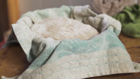 Bread-Dough-Resting-In-A-Basket-Covered-In-Towel-On-Top-Of-A-Wooden-table