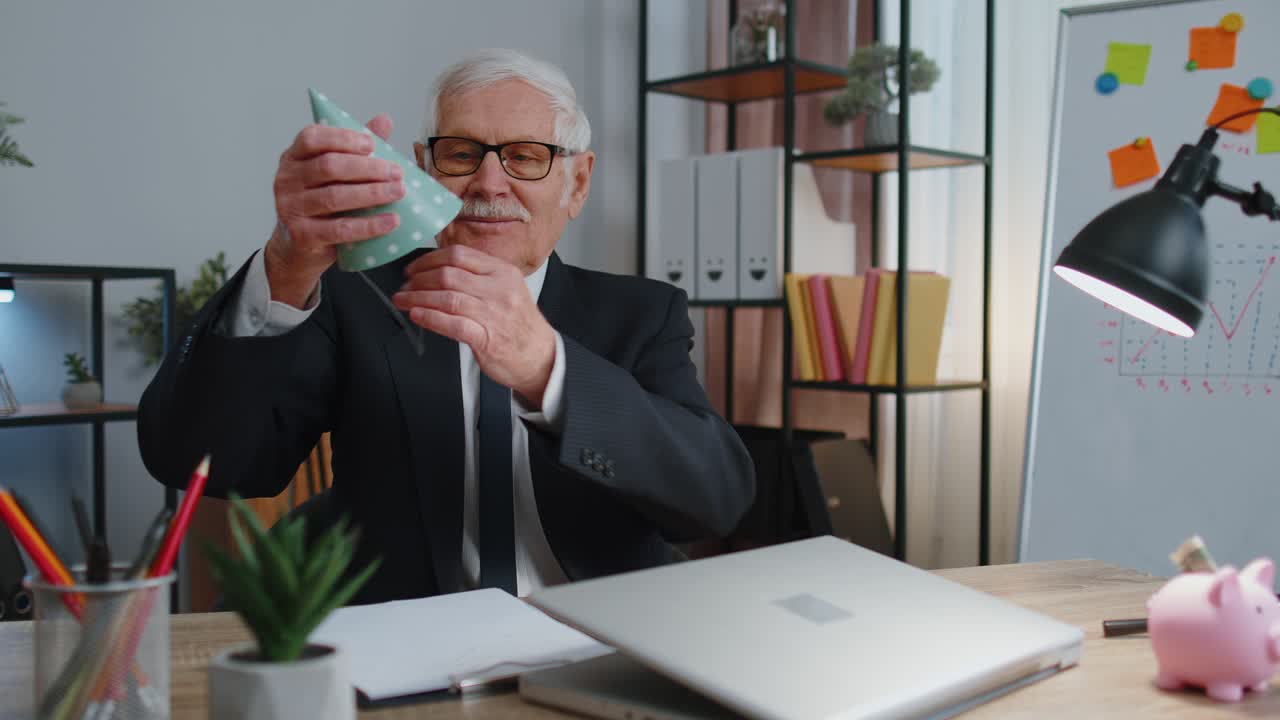 Senior businessman celebrating lonely birthday in office blowing candle on small cake making a wish