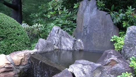 Una-Cascada-Bordeada-De-Rocas-En-Un-Jardín