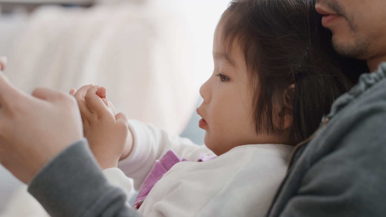 아버지와 함께 아름다운 작은 아시아 소녀가 스마트폰을 사용하는 가족 시간을 보내고 집에서 딸과 함께 휴식을 취하고 있습니다. 4k