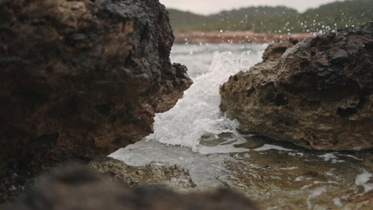 Wave crashes through rocks at the beach, slow motion, low gimbal zoom in