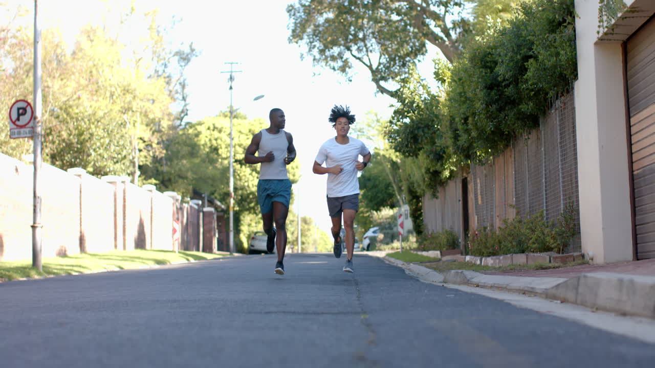 Running, two multiracial male friends exercising outdoors on sunny day in neighborhood, copy space