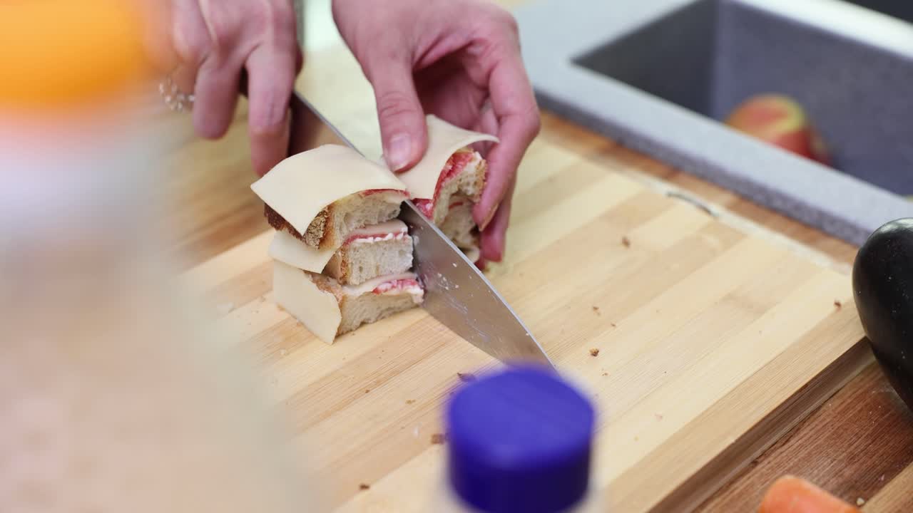 Hands cutting small sandwiches with cheese and filling on a wooden board