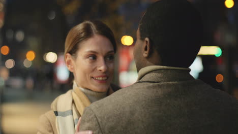 rear view of young african american man hugging a caucasian smiling woman in the street in the evening