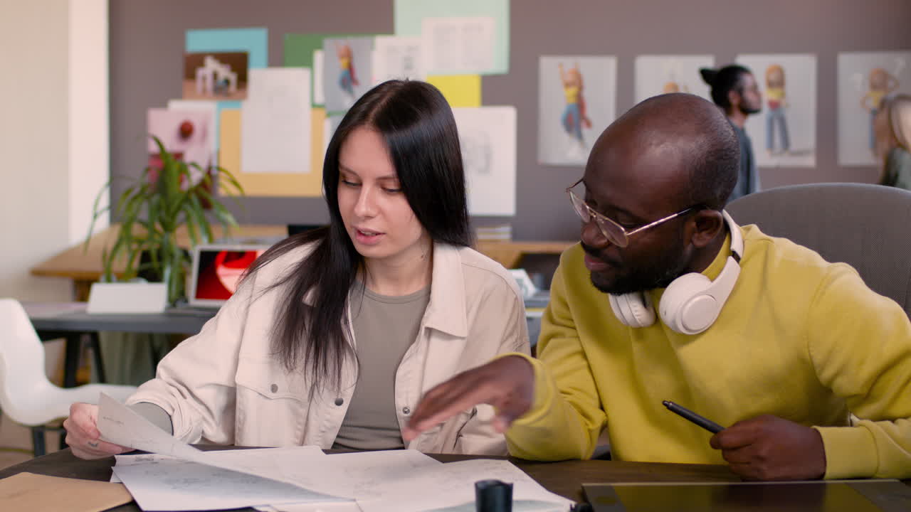 retrato de un hombre y una mujer mirando bocetos mientras están sentados en el escritorio en un estudio de animación