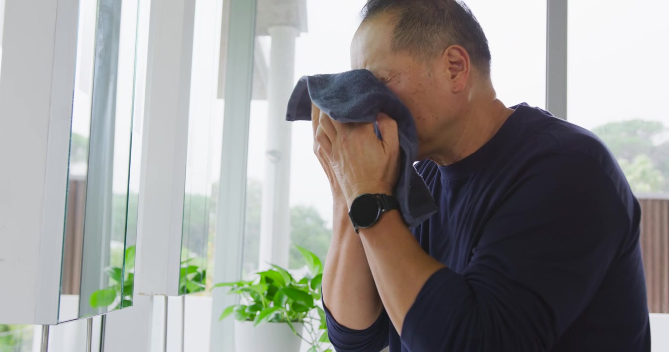 Senior Chinese man starting morning at sink, cupping water, splashing face, drying with blue towel