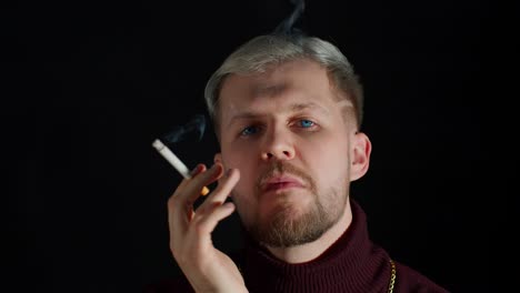 stylish addicted young man with blue eyes in trendy clothes looking at camera, smoking cigarette