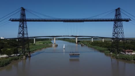 aproximación aérea al puente de transporte en rochefort sur mer, francia. plataforma suspendida cruzando el río y velero en el fondo.