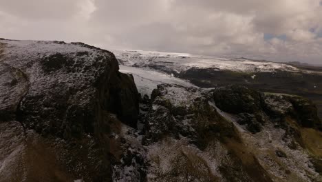 Aerial-revealing-shot-of-snow-covered-peaks-and-the-melting-Sólheimajökull-glacier,-showcasing-rugged-terrain-and-icy-beauty