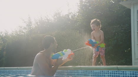 Padre-E-Hijo-Chorreándose-Mutuamente-Con-Pistolas-De-Agua-Jugando-En-La-Piscina-Durante-Las-Vacaciones-De-Verano