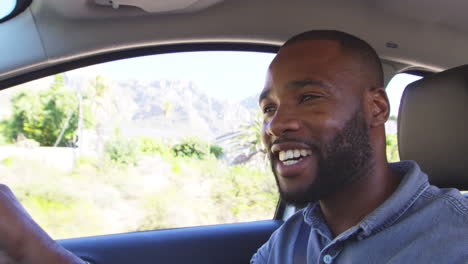 Un-Joven-Negro-Sonriente-Conduciendo-Un-Coche-En-Un-Viaje-Por-Carretera