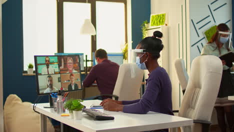 trabajador africano con máscara facial hablando por videocall en la habitación de la oficina