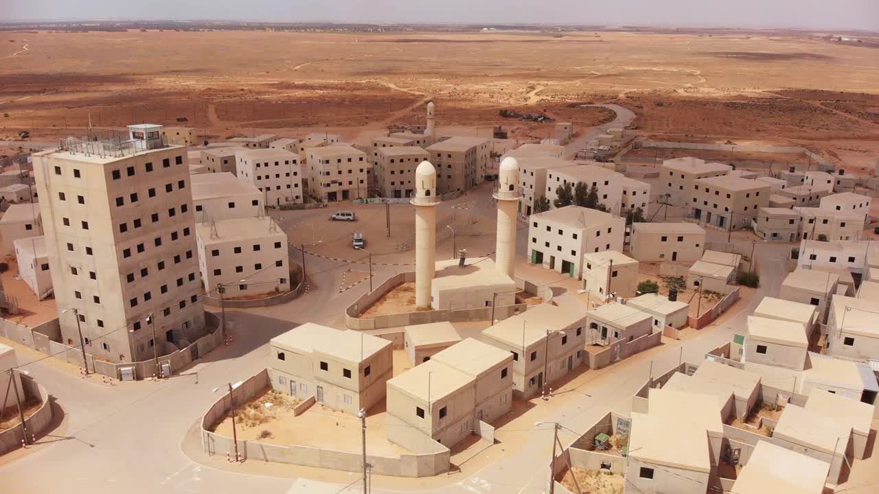 aerial shot of an old empty city in the desert in palestine near Gaza at morning while camera orbit around the buildings and the mosques next to the main squre of the city while a bus driving in it