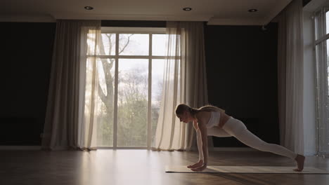 Yoga-Training-In-Einer-Halle-Mit-Großen-Fenstern-Und-Sonnenlicht,-Das-Durch-Den-Rahmen-Fällt.-Eine-Frau-Trainiert-Im-Fitnessstudio-Auf-Einer-Matte