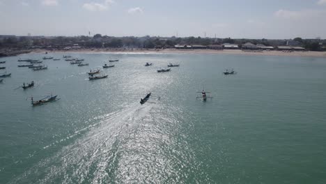 aerial view of indonesian traditional juking boat approaching the beach on turquoise transparent waves near a tropical island of bali