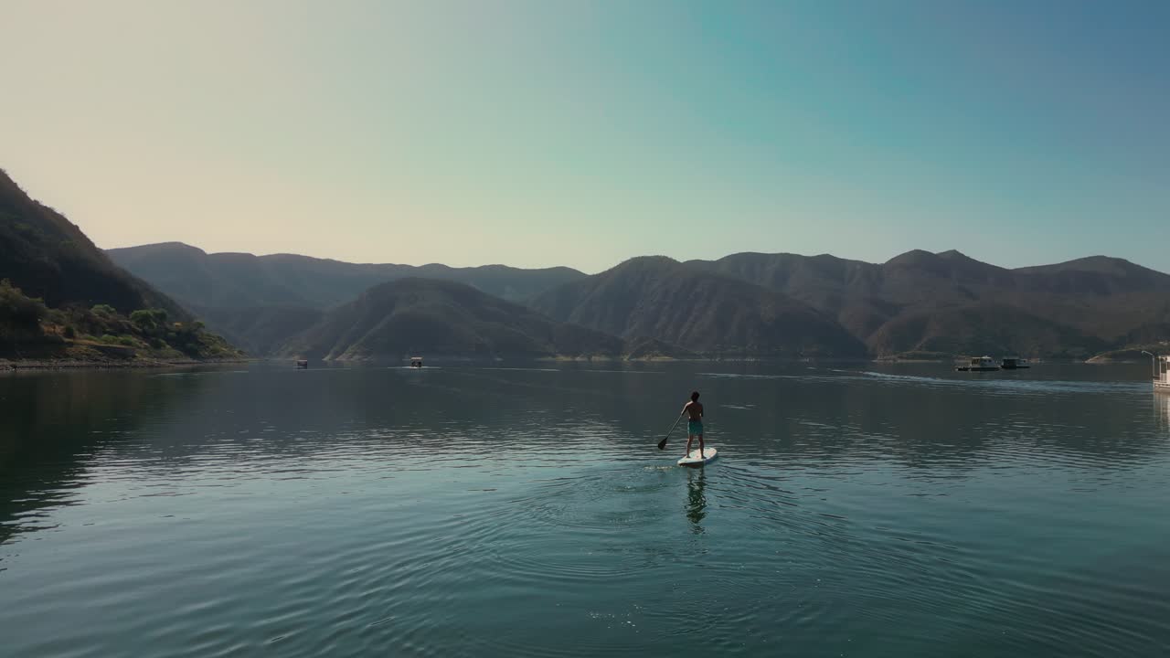 Seseorang Mendayung Papan Dayung di Danau yang Tenang Dikelilingi Pegunungan