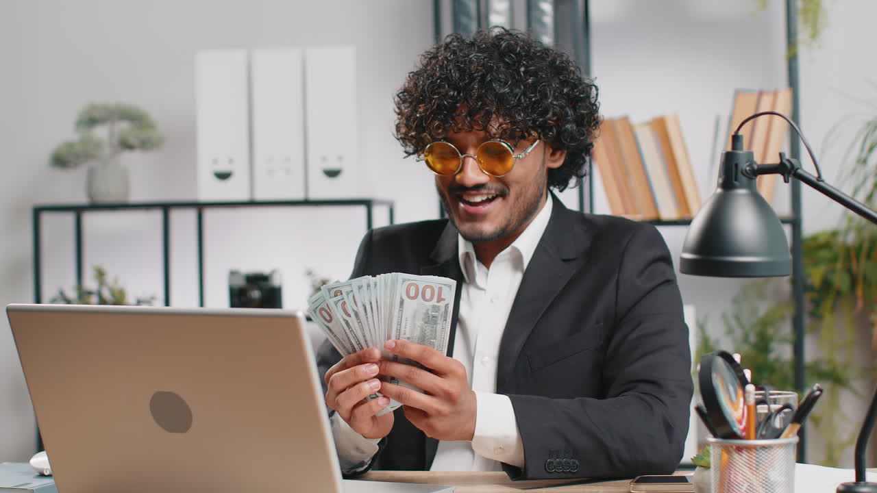 Indian businessman winner holding fan of dollar money cash celebrate dance success career salary