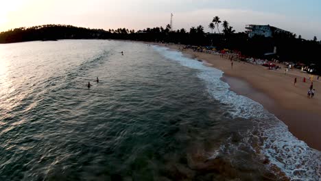 aerial drone over popular and busy tourist beach at sunset in mirissa sri lanka with people swimming