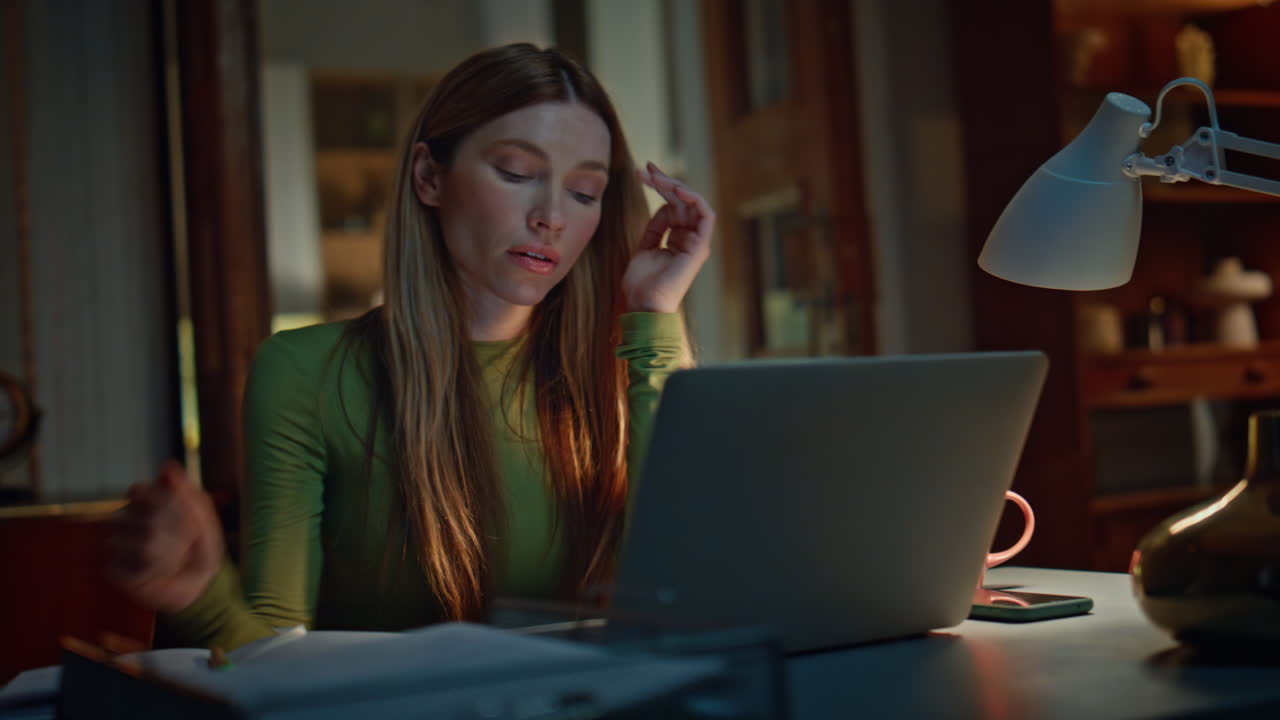 Night worker closing computer feeling overworked in dark apartment close up.