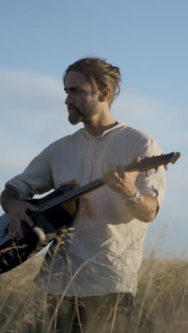 bearded man playing acoustic guitar in a sunny field