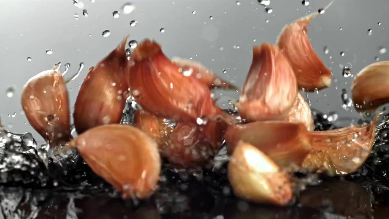 Dentes de Alho Caindo na Água com Respingos em Câmera Lenta.