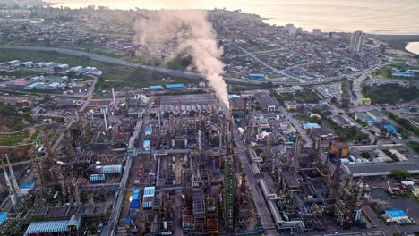 bird's eye view dolly in of an oil refinery with smoking burner, machinery in operation at dusk