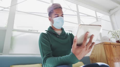 Man-wearing-face-mask-wiping-his-digital-tablet-with-a-tissue