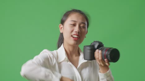 카메라에서 사진을 보는 아시아 사진작가의 클로즈업 골과 춤을 추며 축하합니다. 스튜디오에서 녹색 스크린 배경에 서있는 동안 결과에 만족합니다.