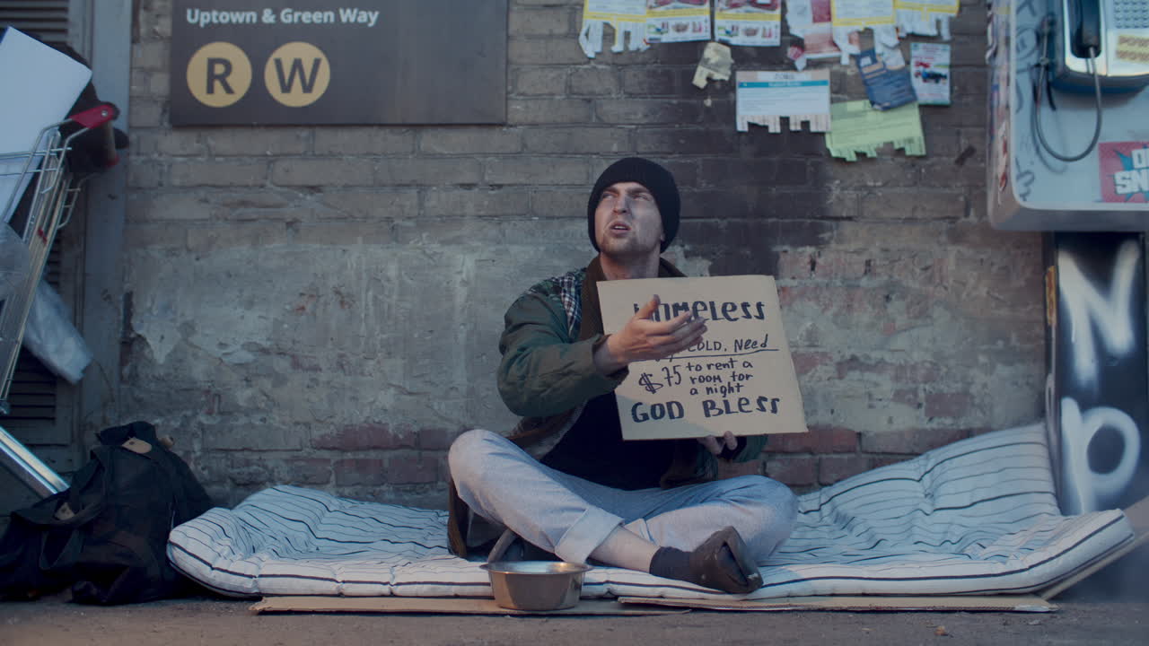 Homeless Man Sitting on Sidewalk, Holding Sign and Begging for Money
