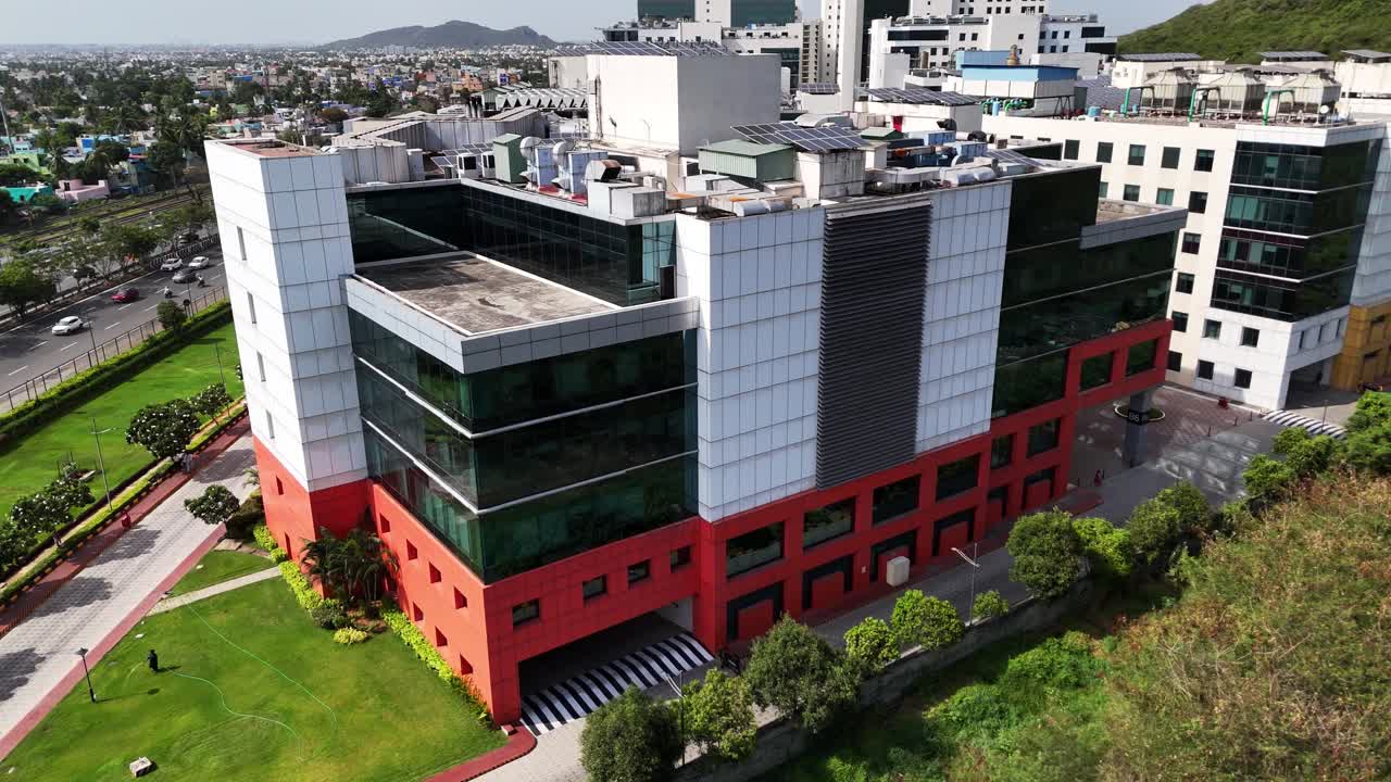 Chennai perungalathur drone footage capturing a sprawling commercial centre contrasting with a natural hillside and a busy urban roadway. Highlights modern architecture and renewable power generation