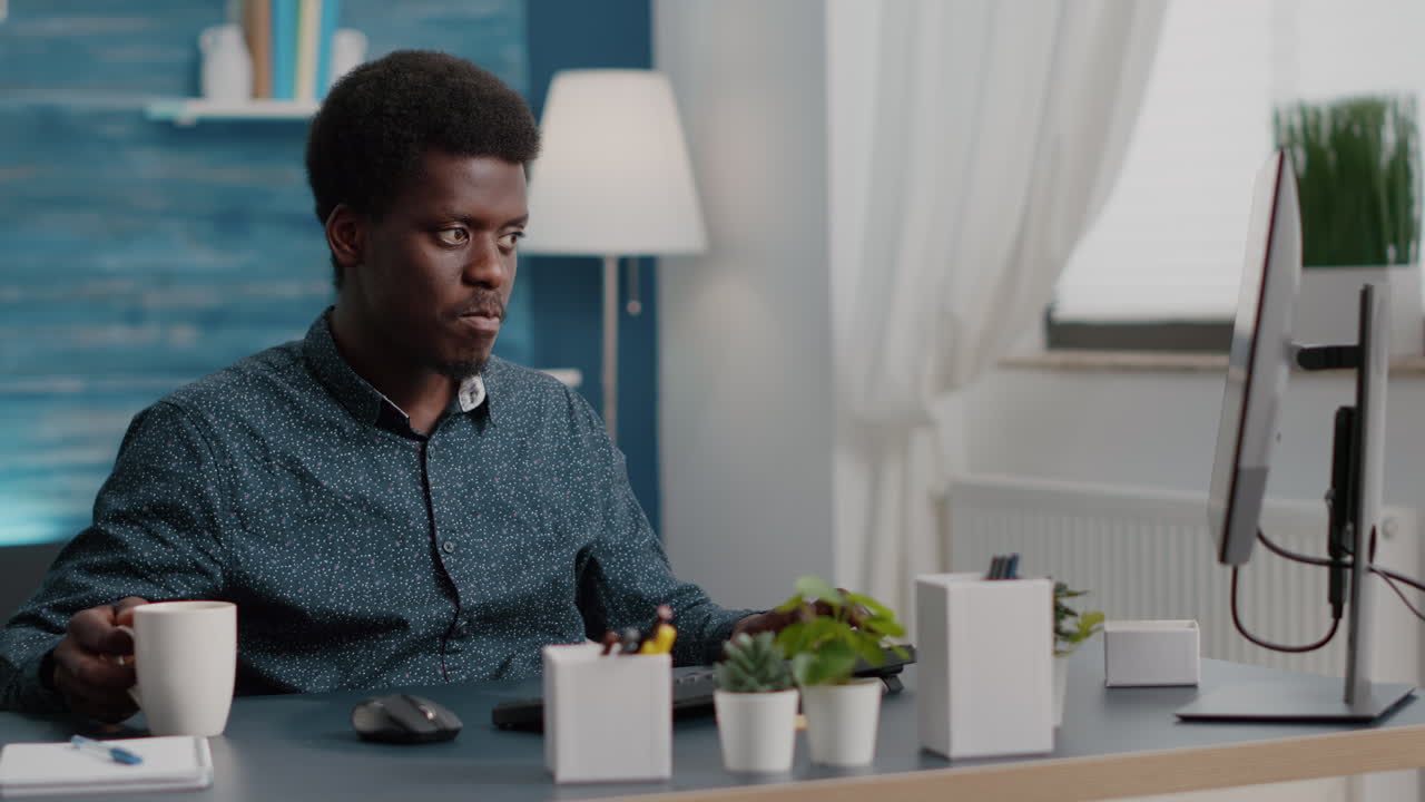 African american manager working from home, sipping coffee and typing on the computer
