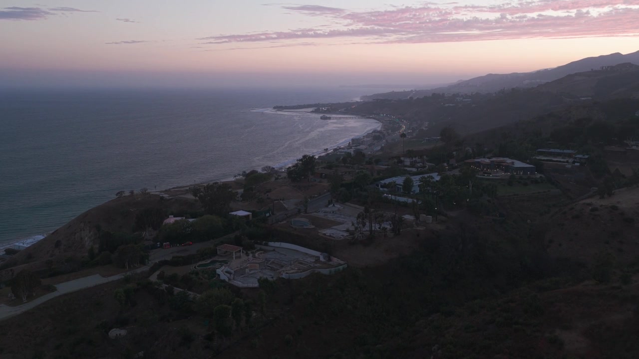 Ripresa aerea ravvicinata in discesa di proprietà bruciate che si affacciano sull'oceano durante il tramonto a Malibu, California. 4K