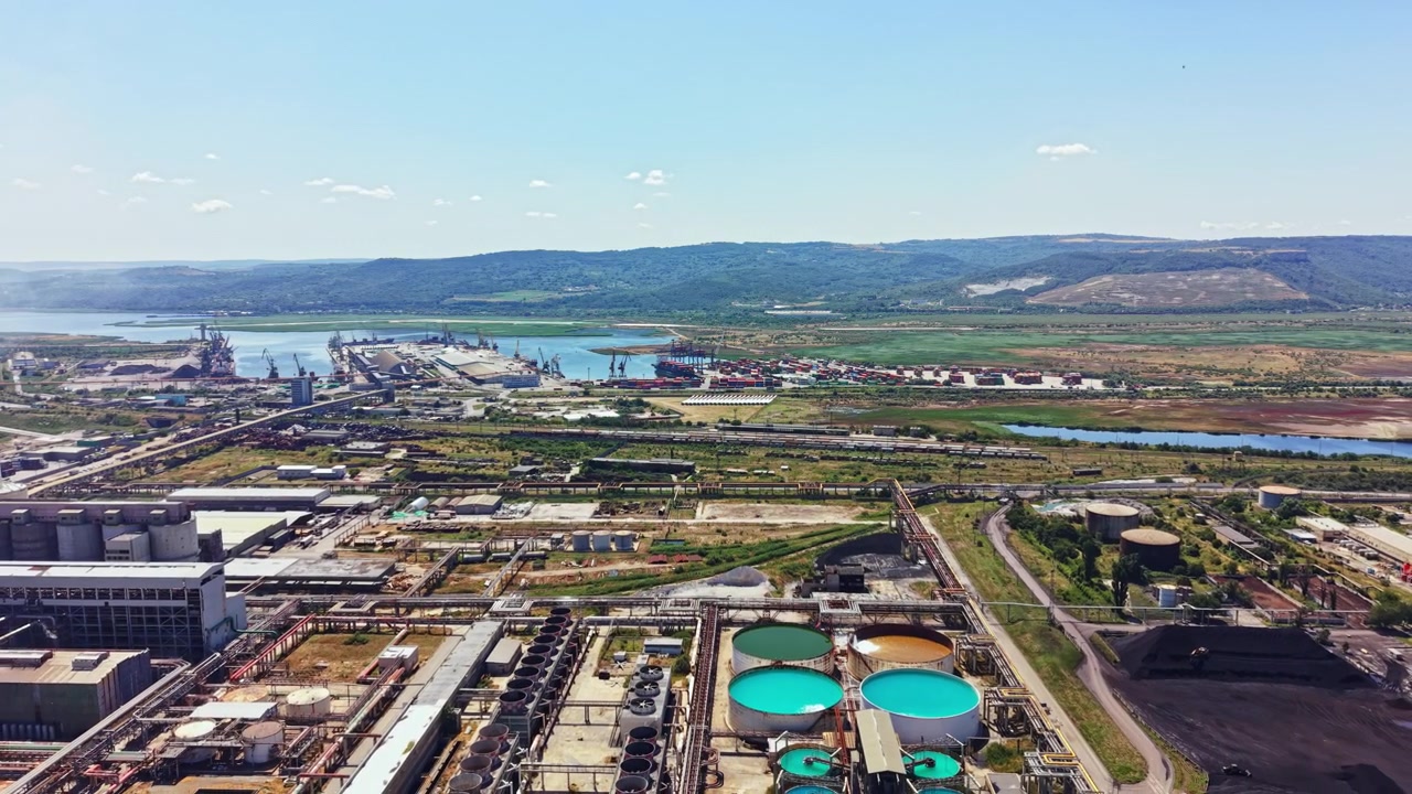 Zona Industrial junto a un Río con Maquinaria, Tanques de Almacenamiento y Área de Envío bajo Cielo Despejado durante el Día