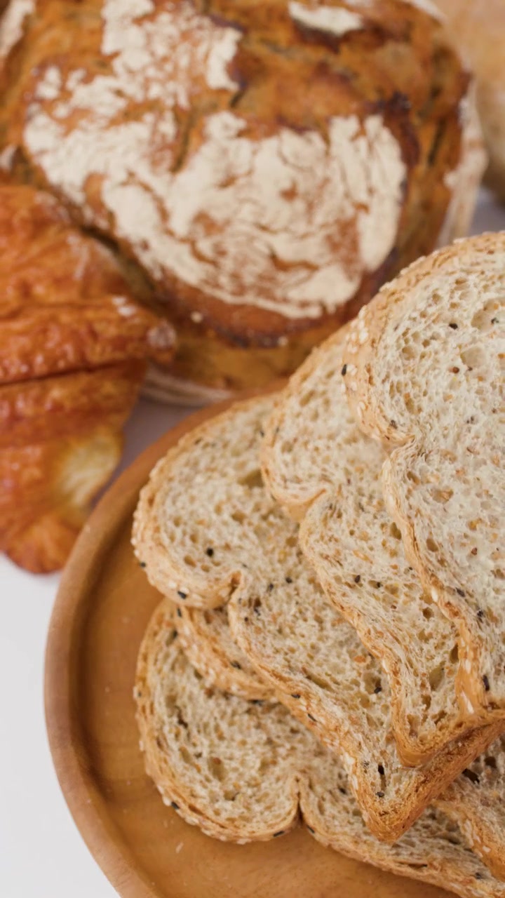 Close-up overhead view of various artisan breads and sliced whole grain toast on white background.