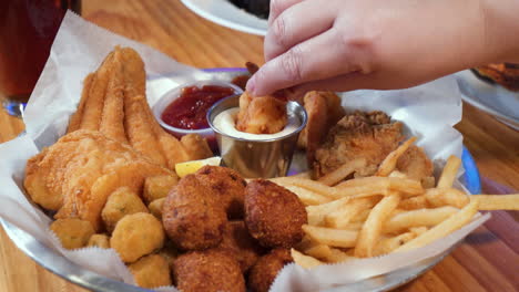 woman's hand picks up shrimp from mixed fried seafood platter and dips into tartar sauce, slider 4k