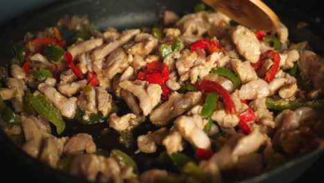 Close-up-of-wooden-spoon-mixing-fajitas-ingredients-cooking-in-pan