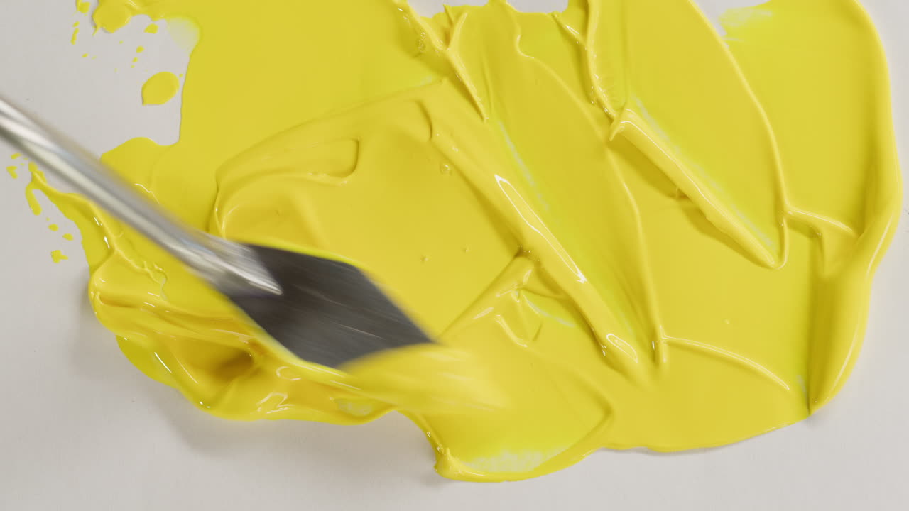 Palette Knife Spreading Bright Yellow Paint on White Surface