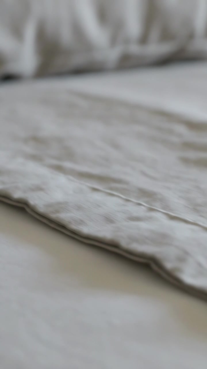 Vertical video: Panning camera filming low-angle duvet seam in bedroom, showing sheet stitching