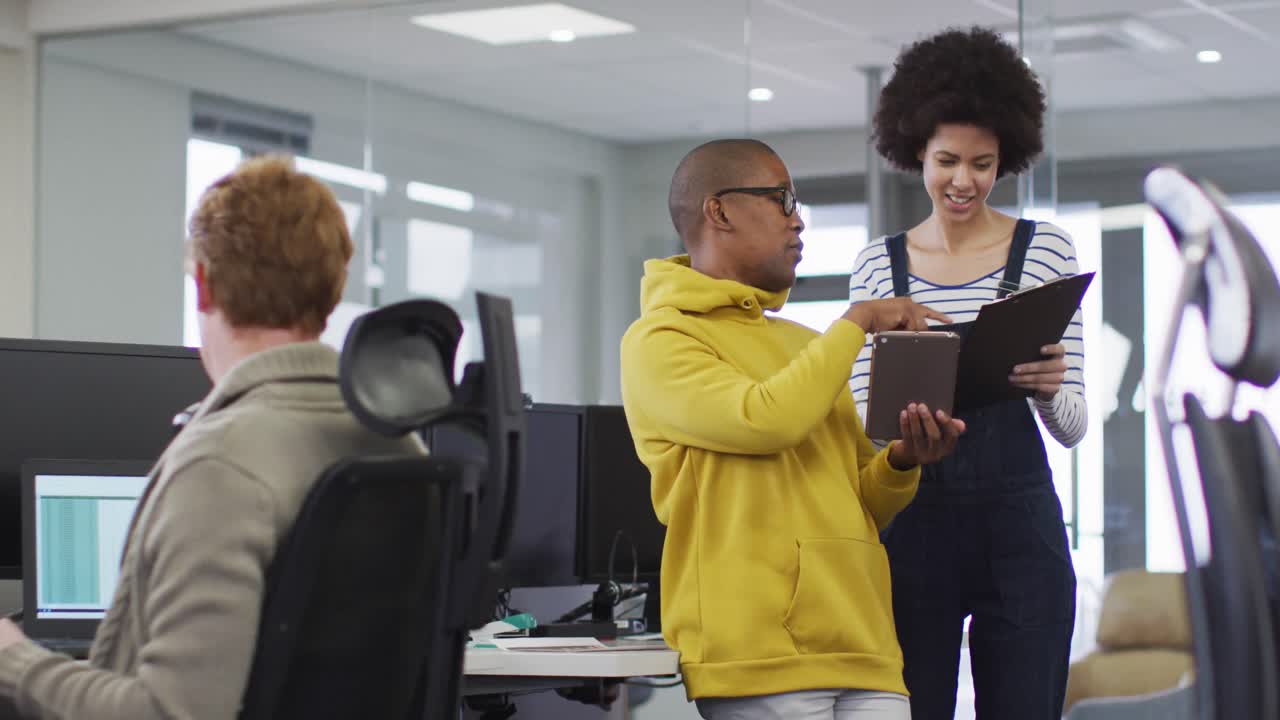 Diverse smiling male and female business colleagues using tablet and discussing paperwork in office