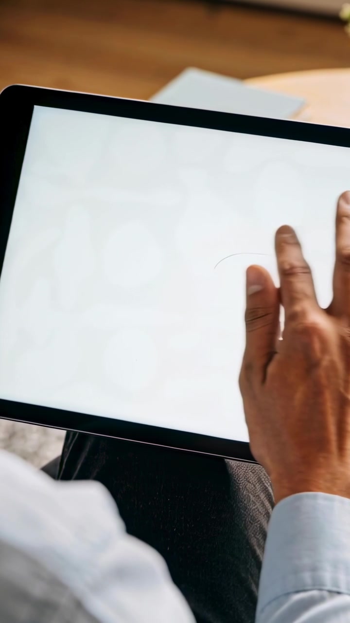 Video verticale: Uomo in camicia blu che tocca e testa lo schermo vuoto di un tablet scorrendo e picchiettando sulle ginocchia