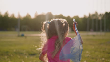 playful little girl with scoop net runs along meadow