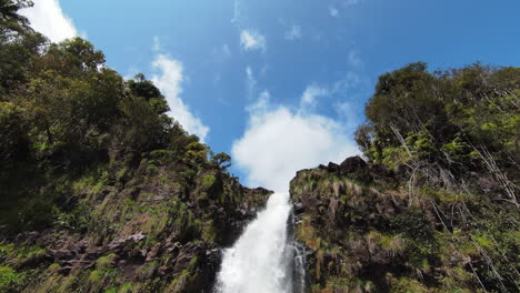 fpv drone vuela hacia arriba, sobre una cascada que cae sobre un acantilado en la jungla hawaiana