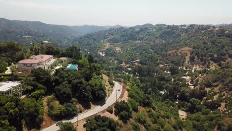 Traffic-on-road-in-Beverly-Hills-at-sunset-with-luxury-mansion-and-swimming-pool