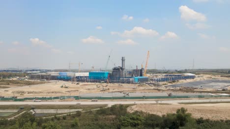 massive construction site with cranes rising in horizon, aerial tracking view