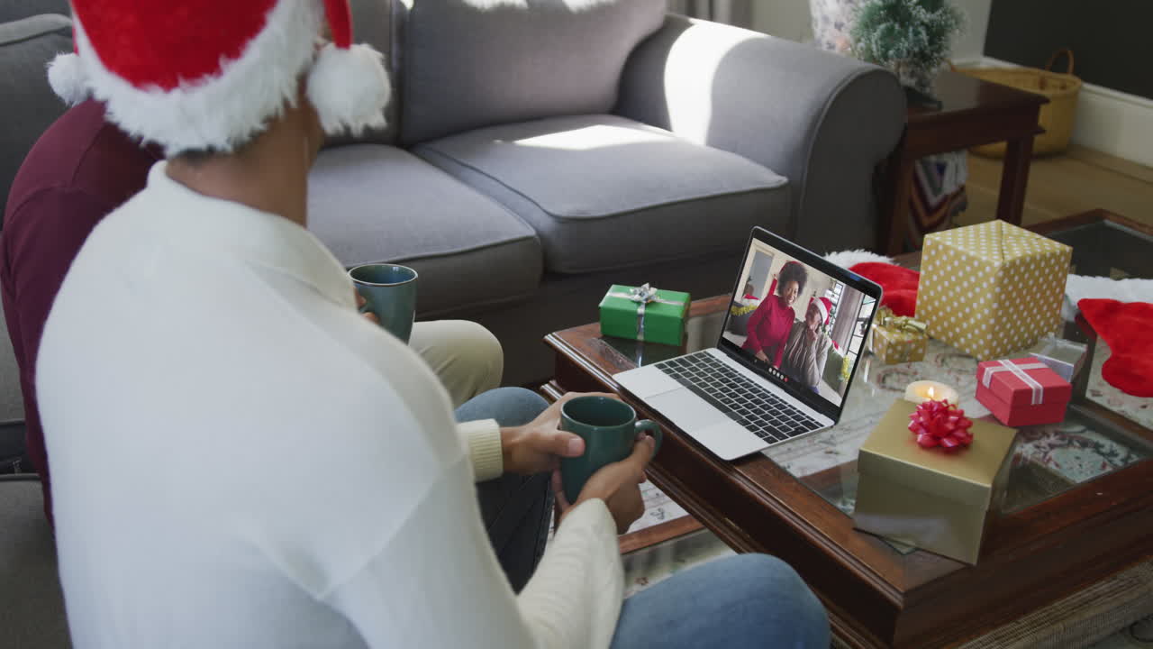 padre y hijo biraciales usando computadora portátil para una videollamada de navidad con familia feliz en la pantalla