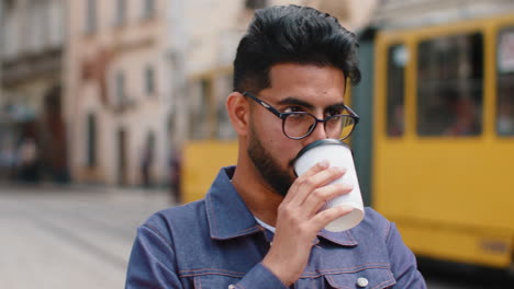 young indian man enjoying drinking morning coffee hot drink relaxing taking a break in city street